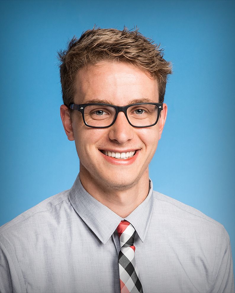 Business headshot of a man in glasses and a tie, on a blue backdrop