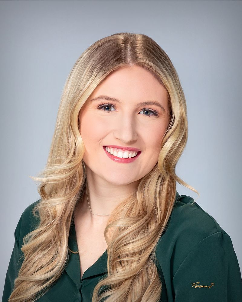Business headshot of a woman in a green blouse, on a gray backdrop