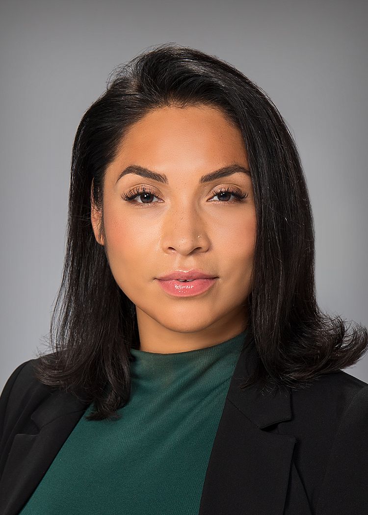 Business headshot of a woman in a black blazer, on a gray backdrop