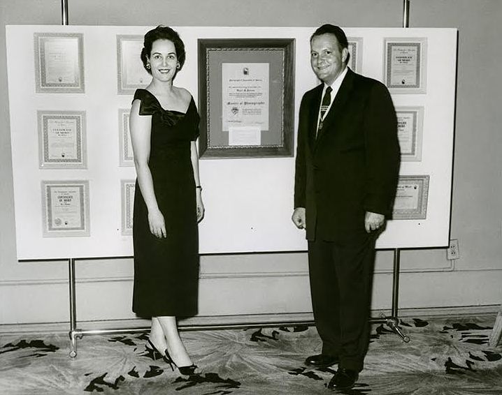 Wayne and Lorene Parsons standing beside framed awards in the original studio