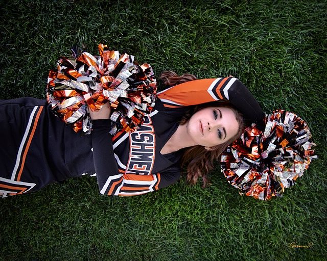 Cheerleader lying on the grass between orange and black pom-poms