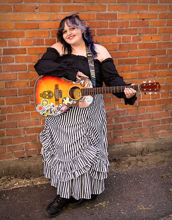 Senior holding an acoustic guitar in front of a brick wall