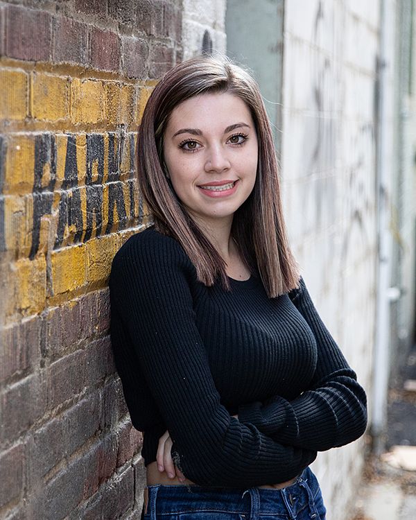 Senior leaning against a painted brick wall