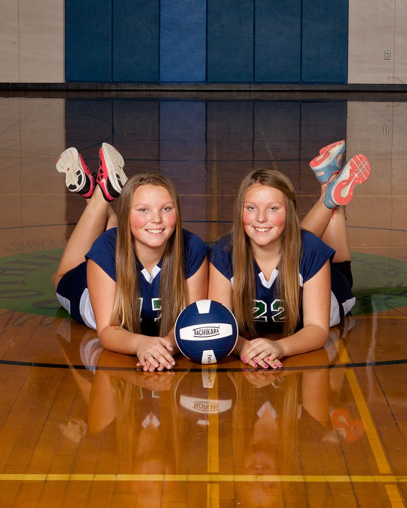 Two volleyball players lying on the gym floor with a ball between them