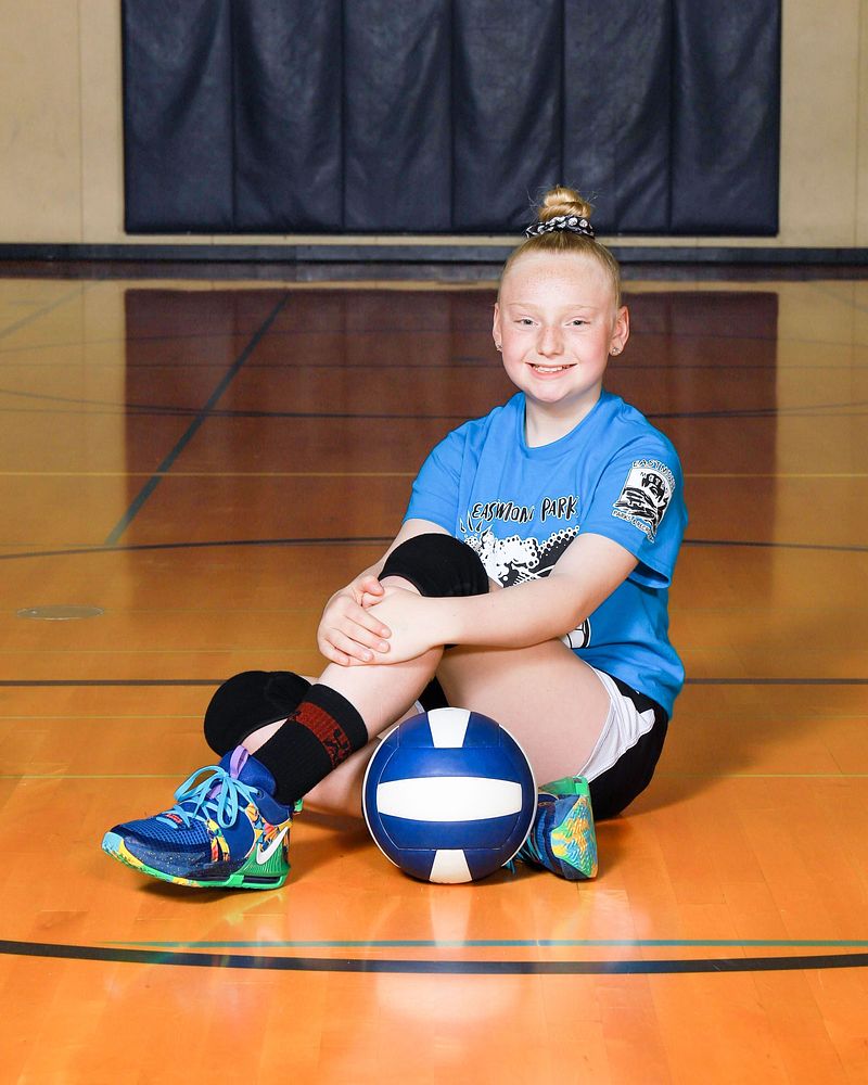 Young volleyball player sitting on the gym floor beside a ball